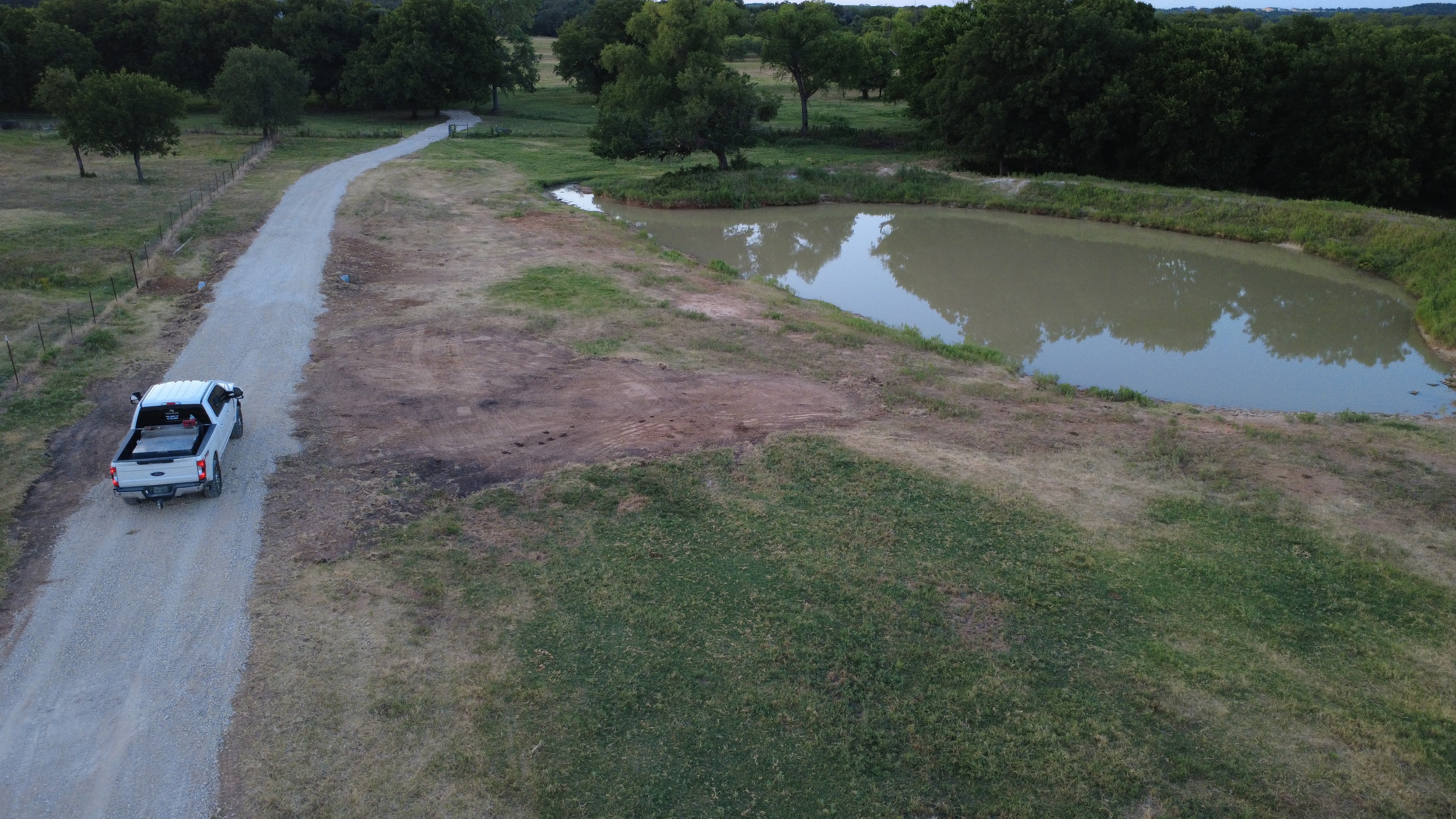 Aerial view of gravel road alongside a pond on rural property