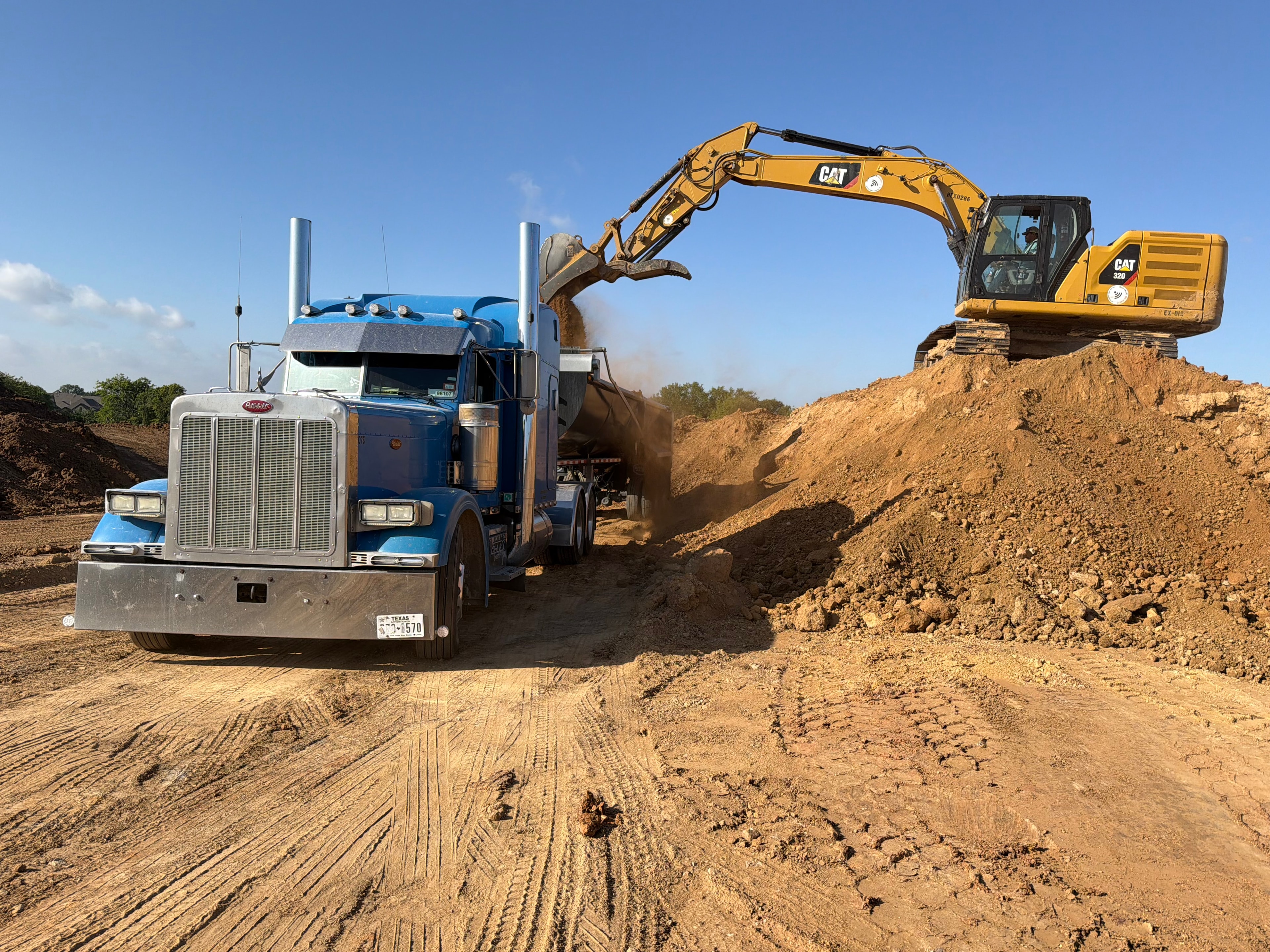 CAT excavator loading blue Peterbilt dump truck on job site