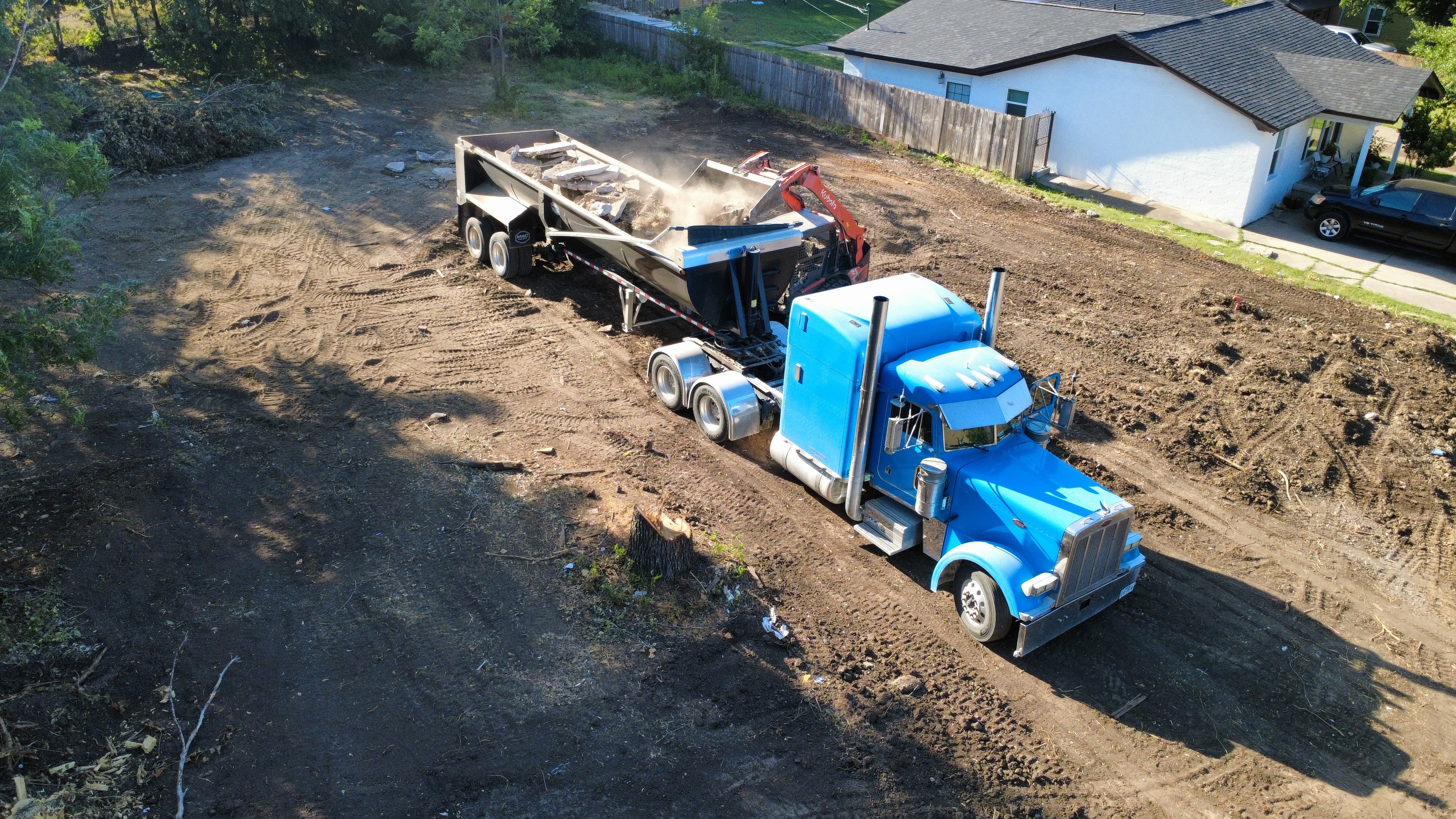 Aerial view of blue dump truck and excavator clearing a residential lot